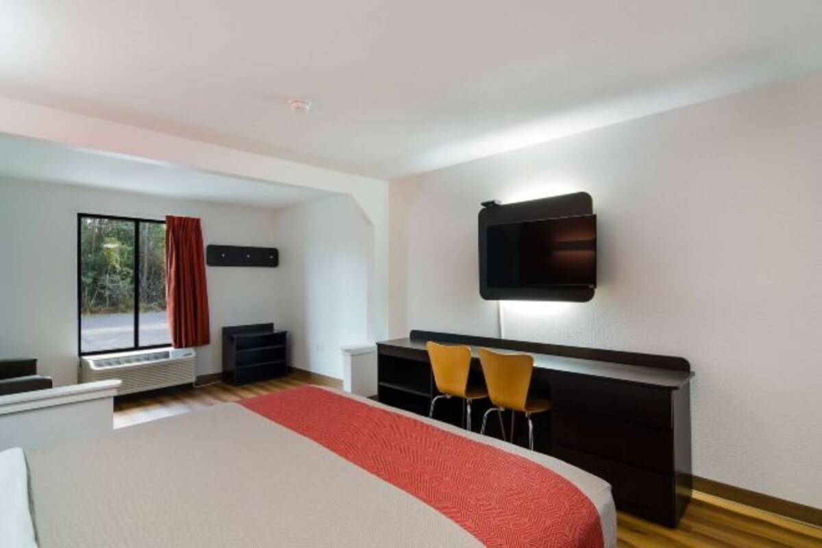A hotel room with a large bed, a TV mounted on the wall, a desk with two chairs, and a window with a view of trees.