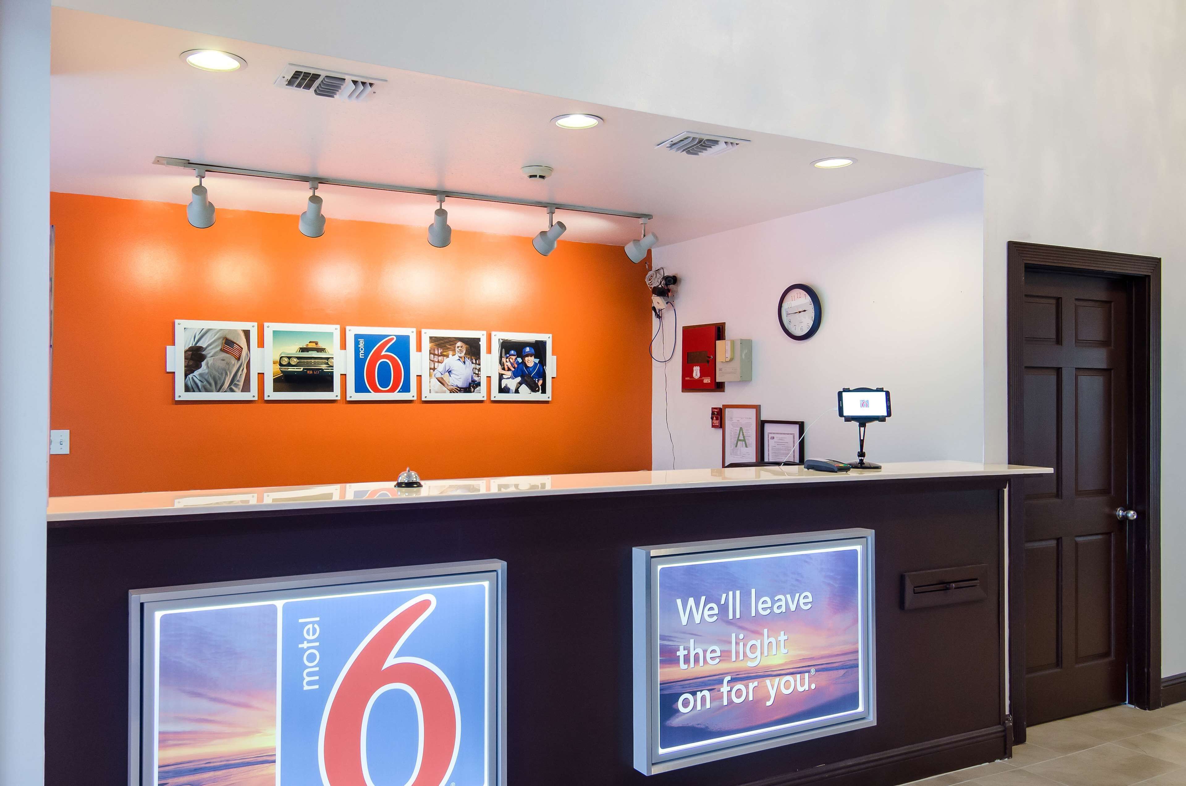 Un comptoir d’accueil d’hôtel avec une grande enseigne lumineuse indiquant « Motel 6 » et un message disant : « Nous laisserons la lumière allumée pour vous. »