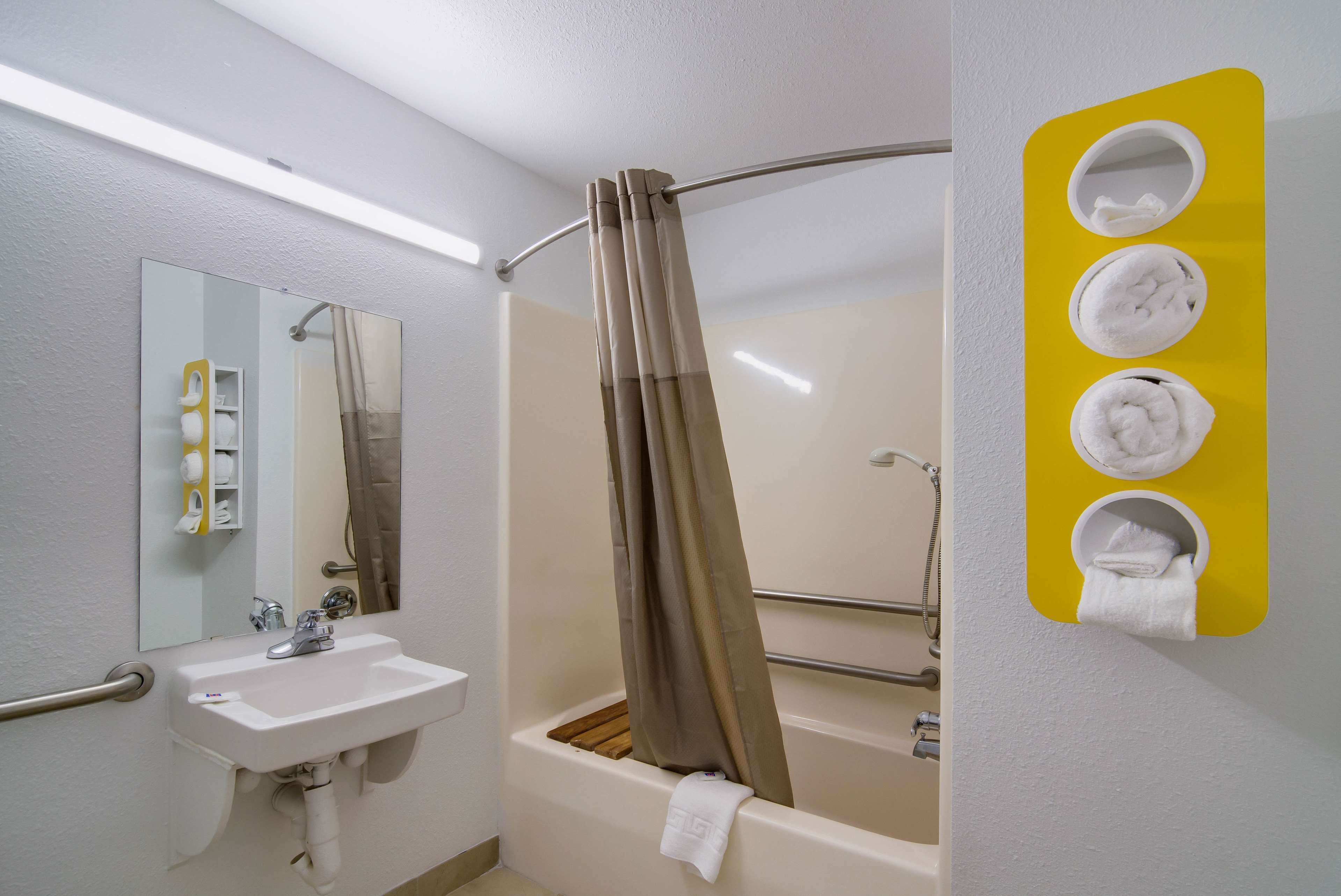 Een badkamer met een wastafel, spiegel, douchegordijn en handdoekhaken.