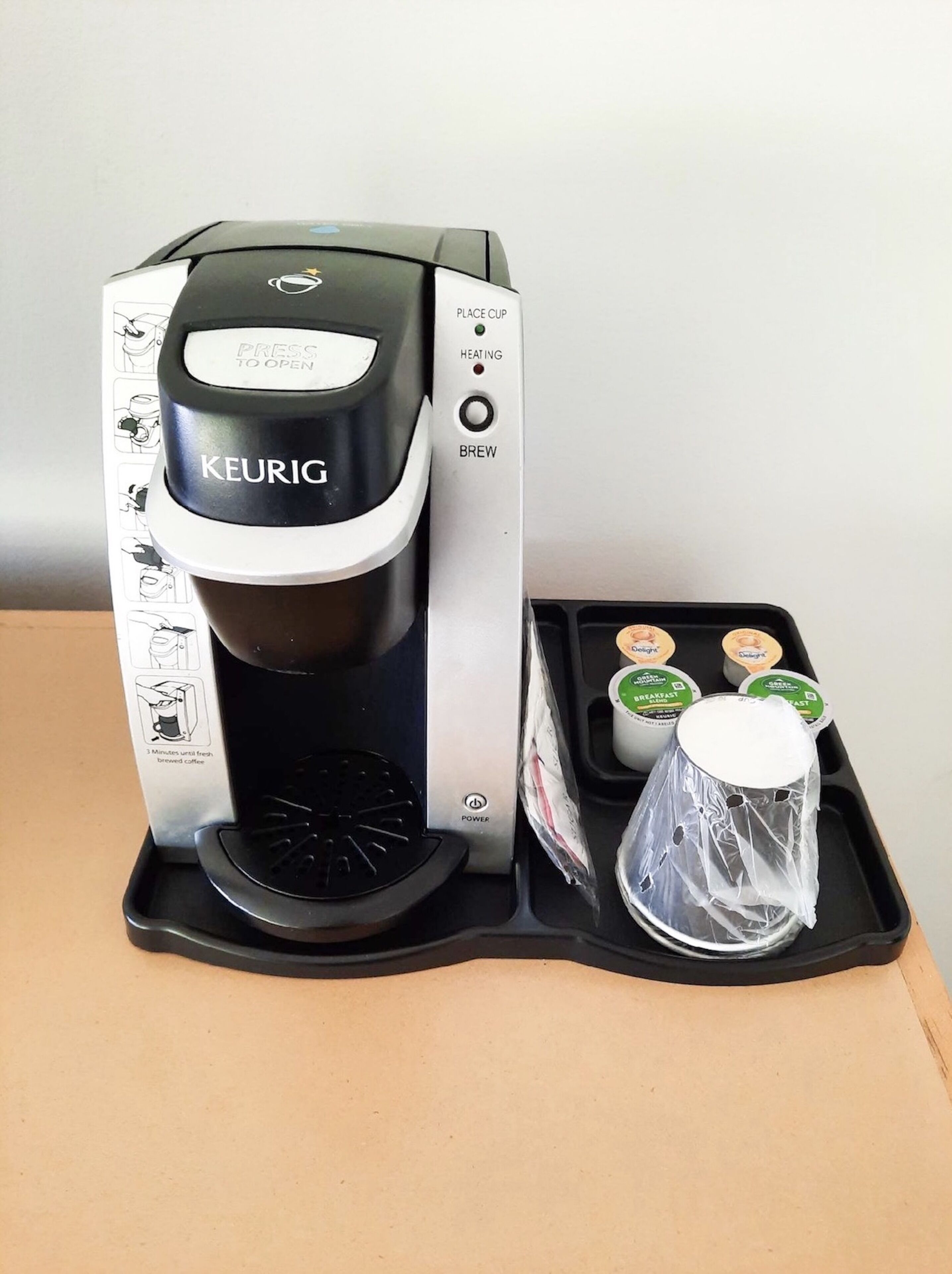 Een Keurig koffiezetapparaat met een dienblad waarop twee herbruikbare bekers en een karaf staan.
