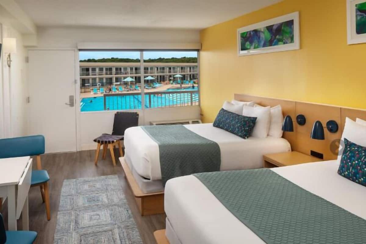 Une chambre d’hôtel avec deux lits, une télévision, un bureau et une vue sur une piscine et un immeuble.