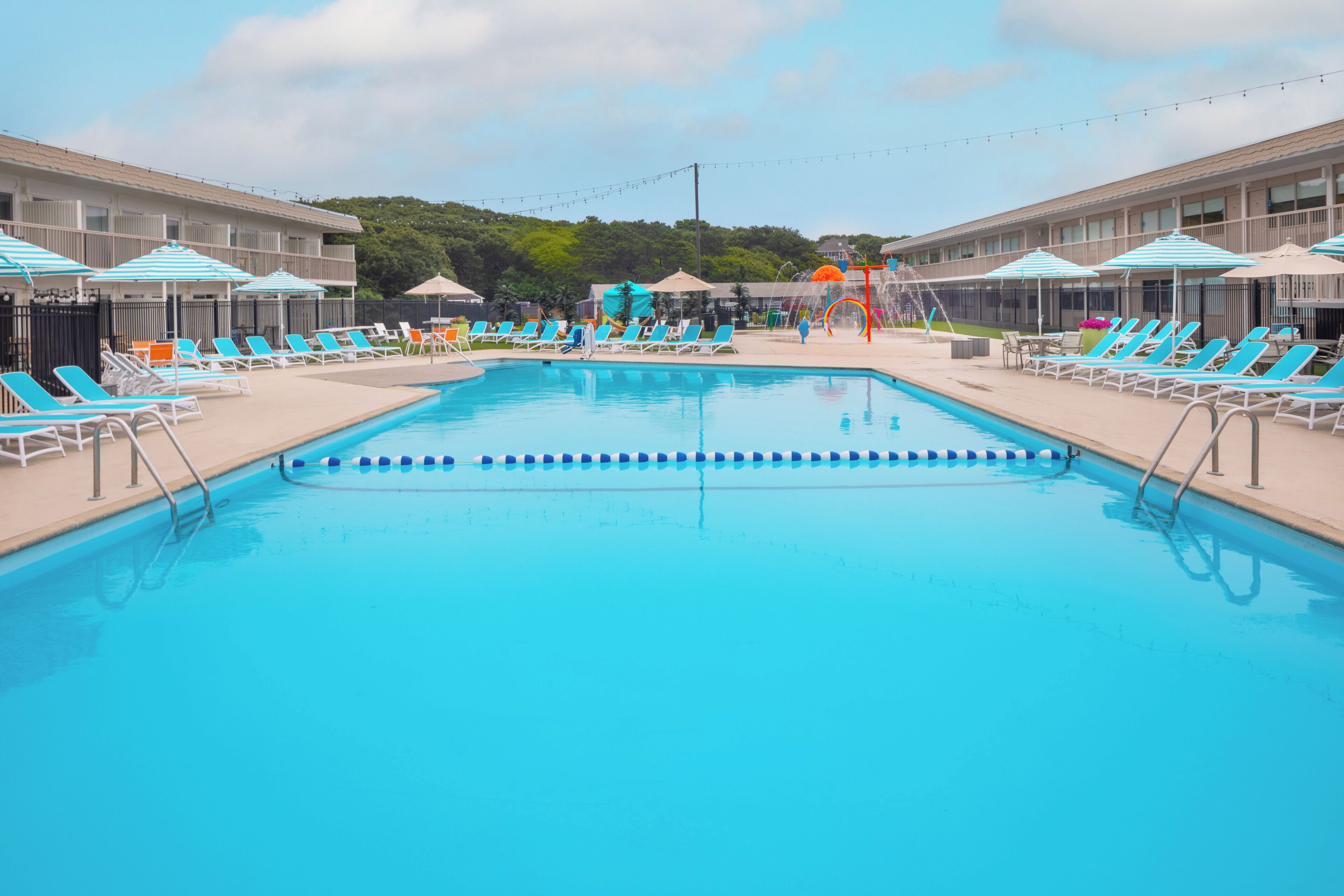 Une piscine entourée d’un bâtiment doté de balcons, avec des chaises longues bleues et blanches et des parasols.