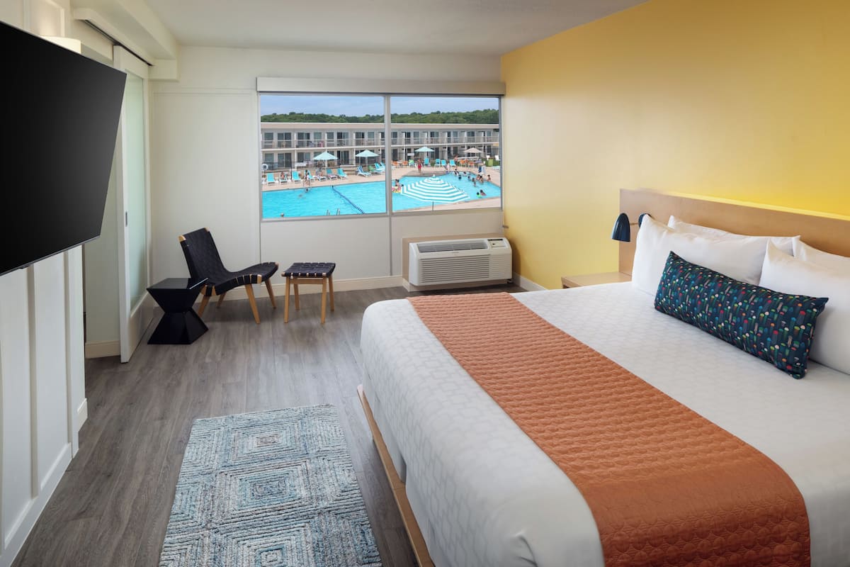 Une chambre d’hôtel dotée d’un grand lit, d’une télévision, d’un bureau avec une chaise, d’une fenêtre donnant sur la piscine et d’un appareil de climatisation.