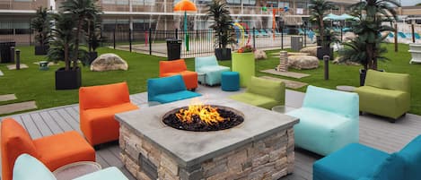 An outdoor seating area with a fire pit, colorful chairs, and a pool in the background.