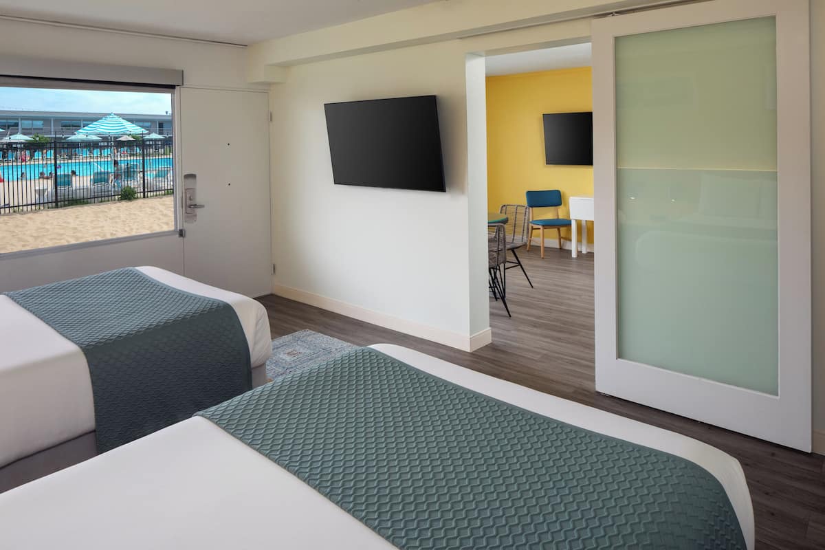 Une chambre d’hôtel avec deux lits, une télévision, une vue sur la piscine et un coin repas avec des chaises et une table.