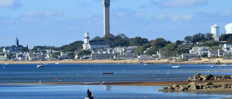 A coastal town with a prominent tower, sandy beach, and boats in the water.