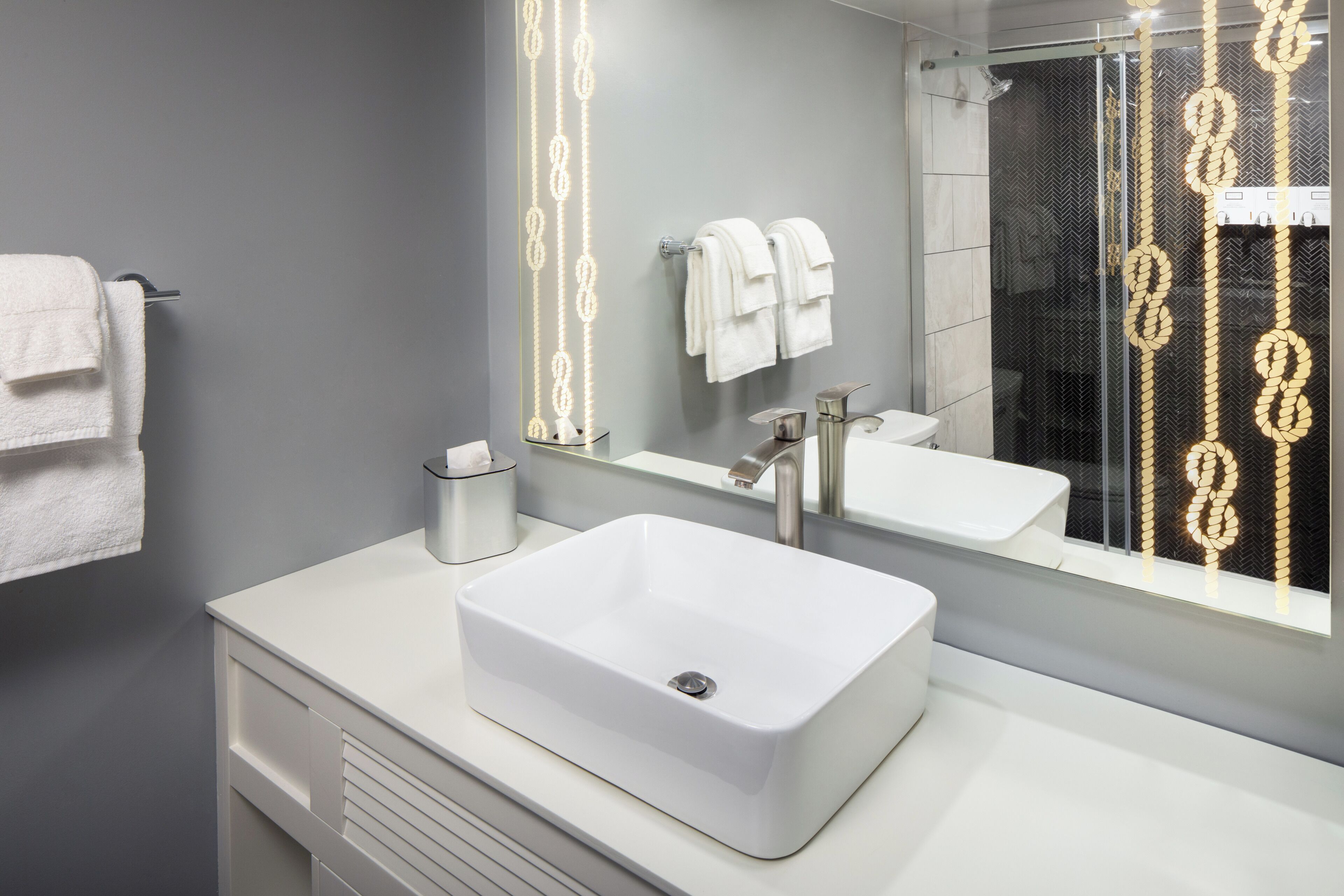 A modern bathroom with a white sink, a large mirror, and a shower area.