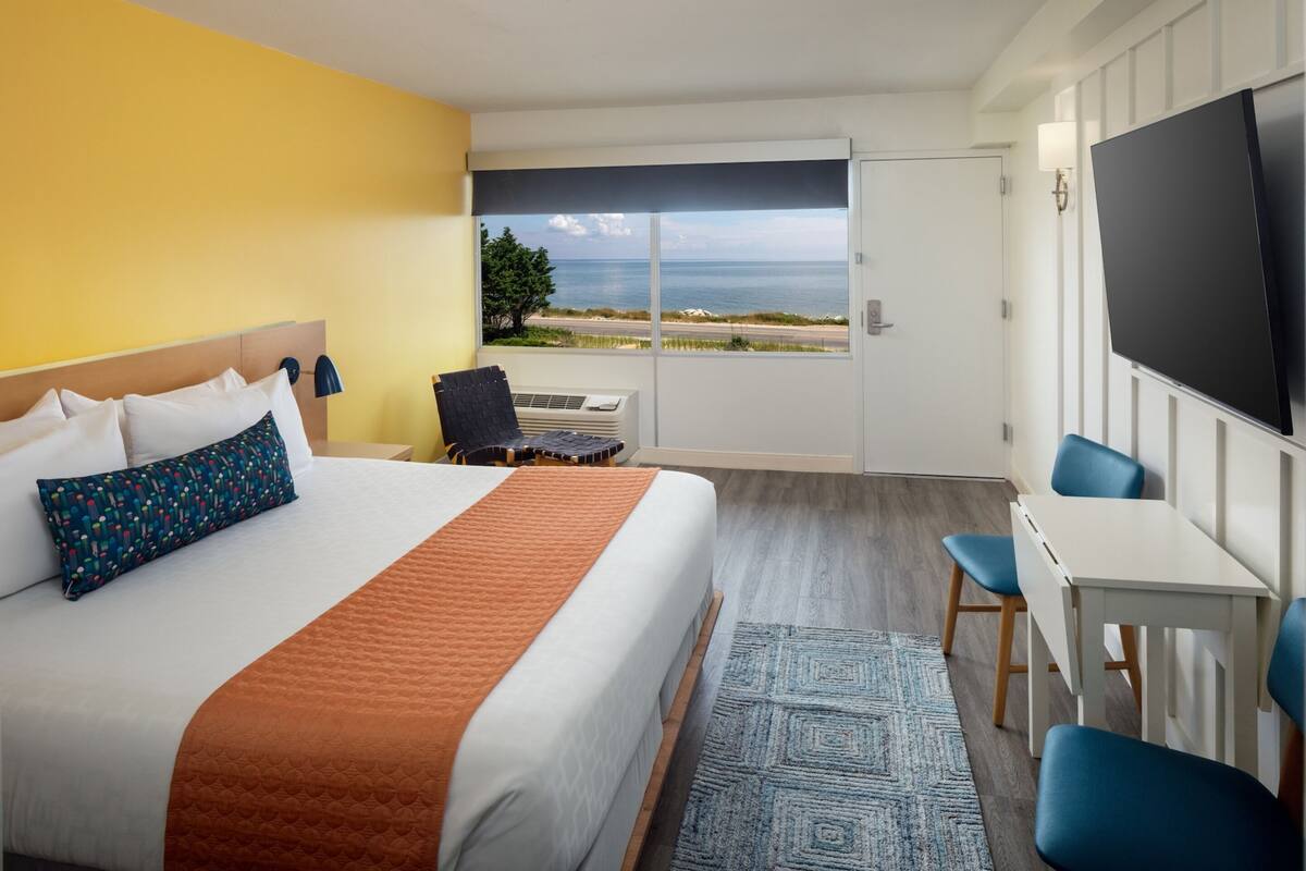 Une chambre d’hôtel avec un lit, un bureau, une télévision et une vue sur la mer.