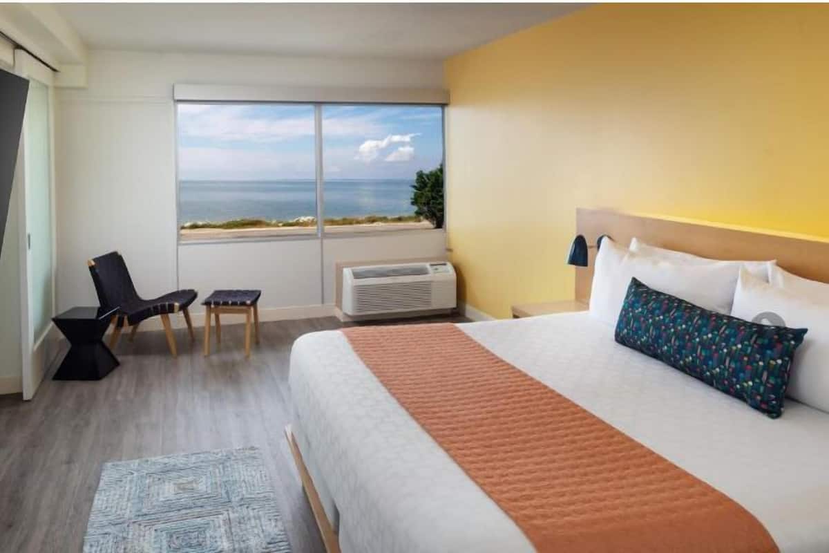 Une chambre d’hôtel avec un grand lit, une télévision, une chaise, une petite table et une fenêtre donnant sur la mer.