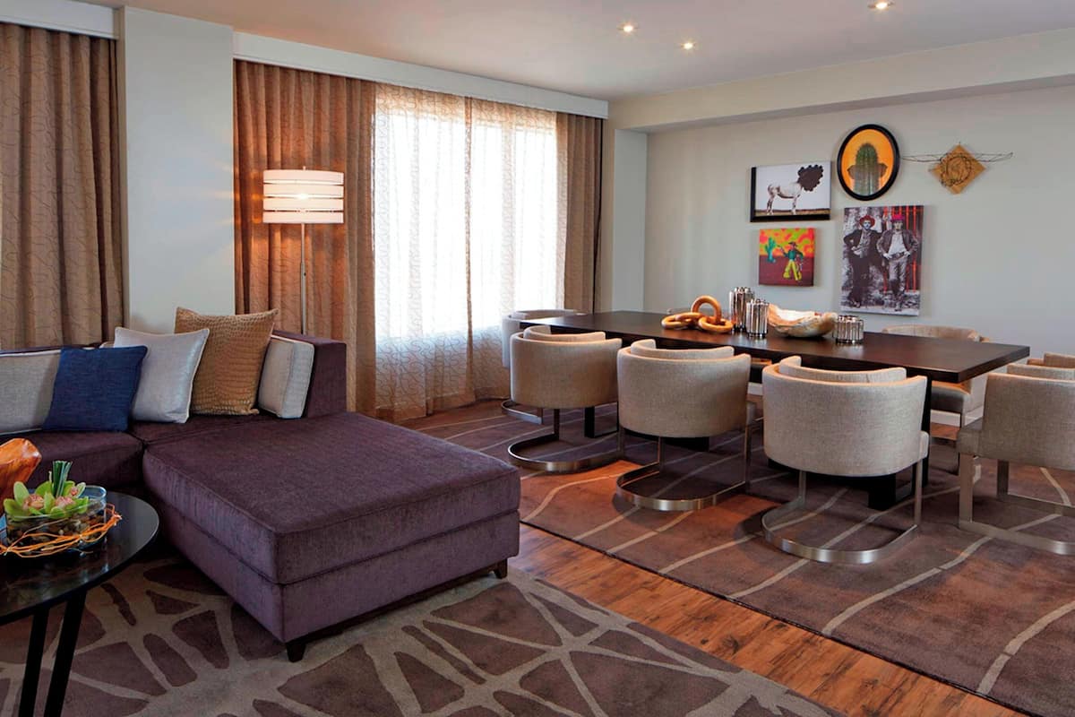 A modern hotel room with a sofa, ottoman, dining table, and chairs.