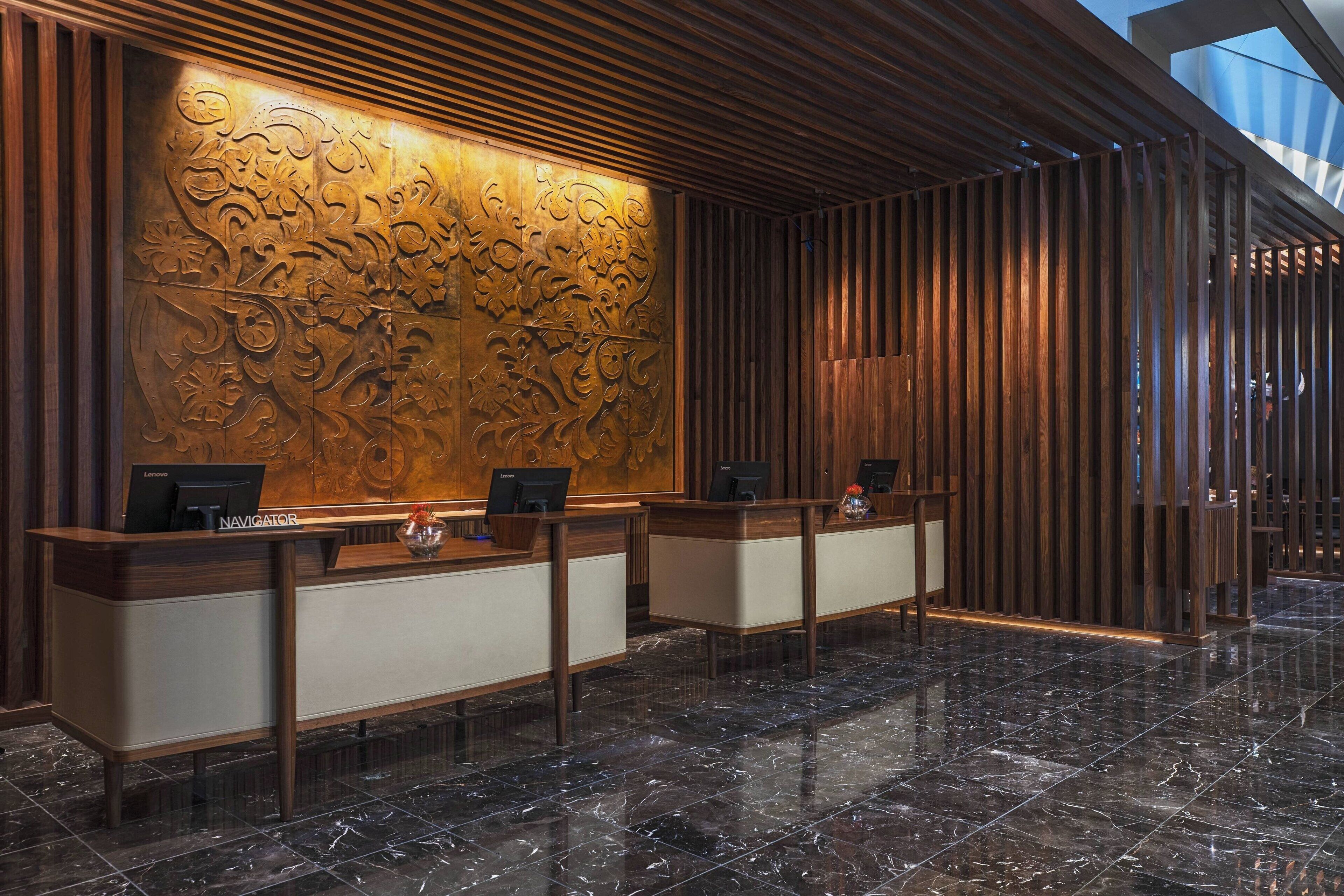 Zona de recepción con diseño moderno, que presenta un mostrador de madera y una pared decorativa con intrincados patrones.