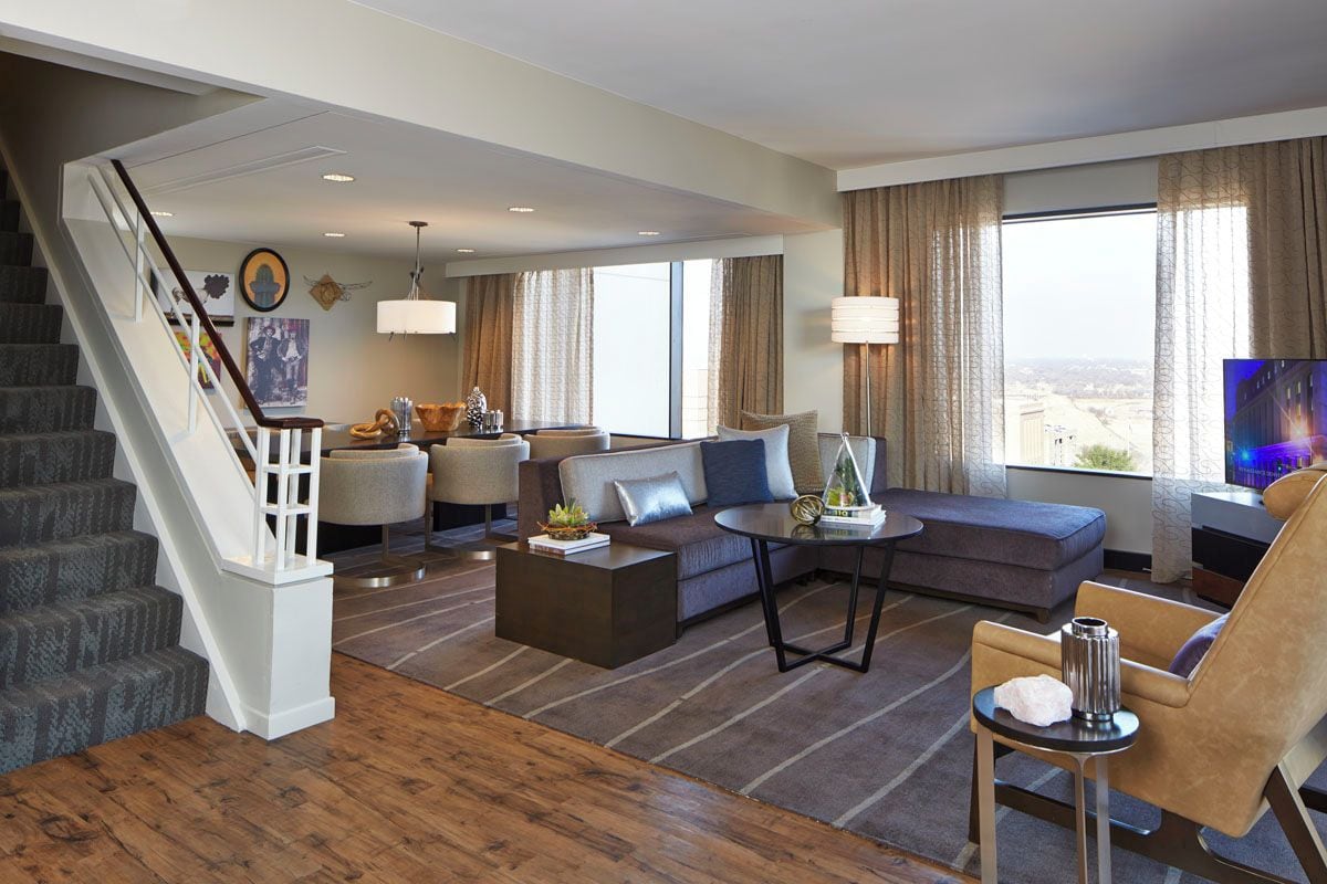 Habitación de hotel con escalera, sofá, mesa de centro, televisor y vista a la ciudad.