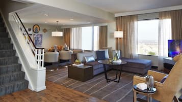 Habitación de hotel con escalera, sofá, mesa de centro, televisor y vista a la ciudad.