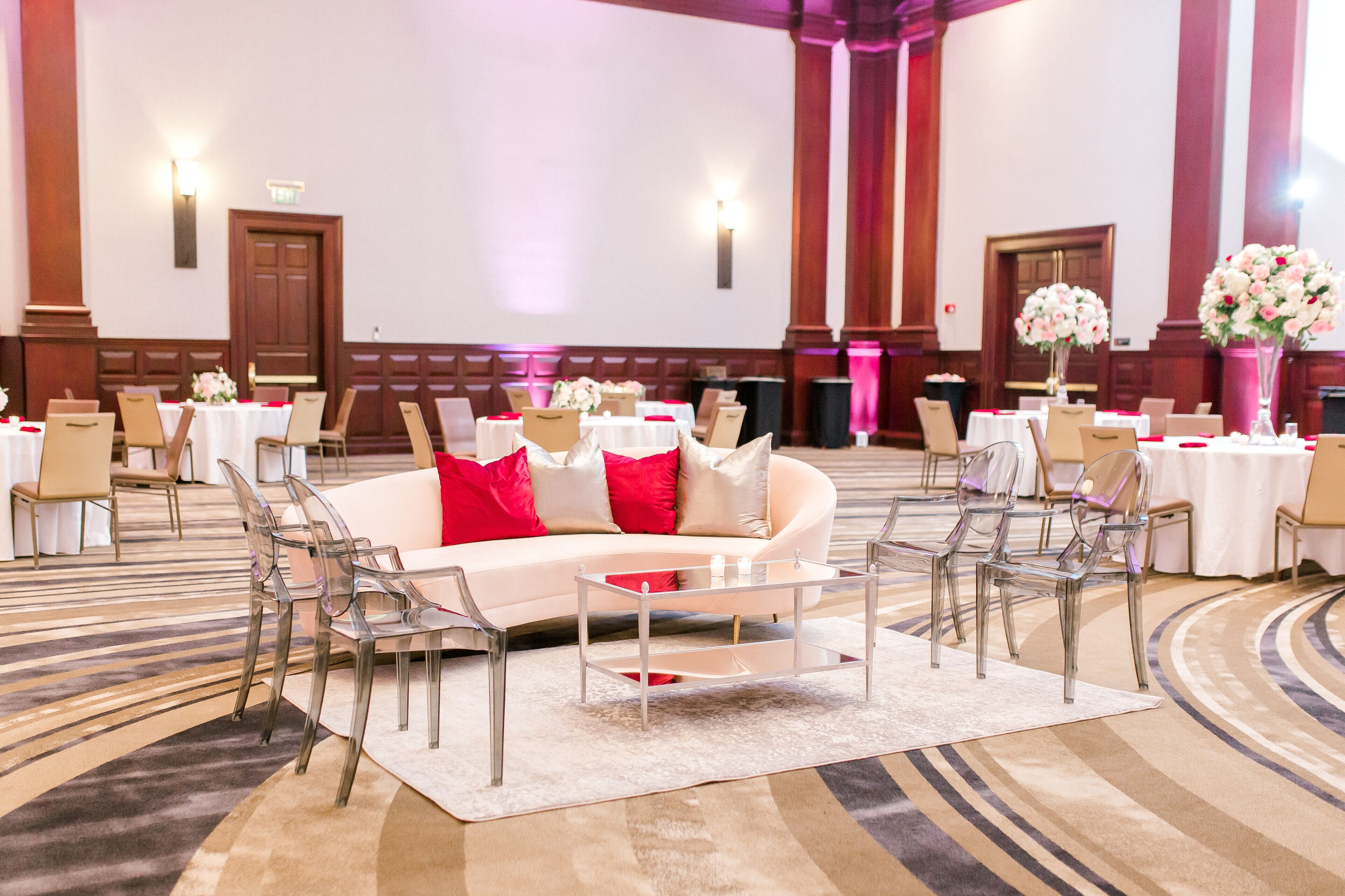 A hotel lobby with a round white sofa, clear chairs, and tables set up for a meeting.