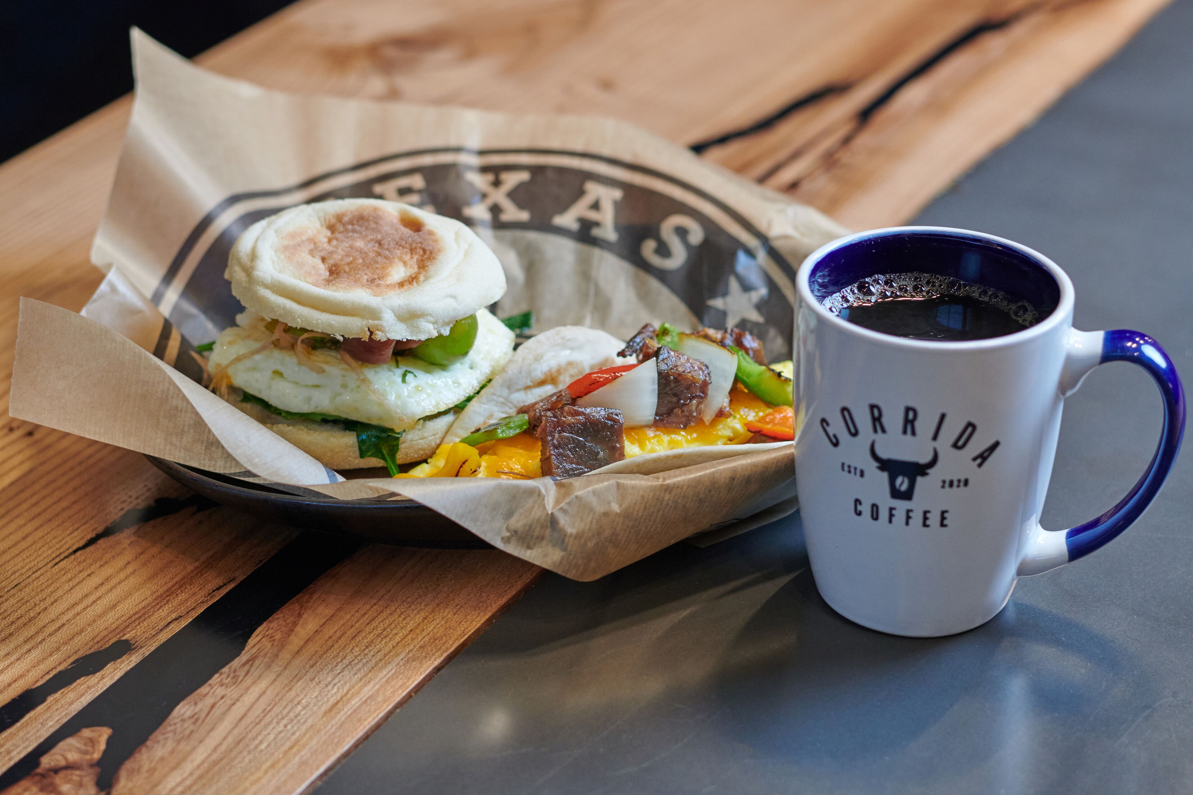 A breakfast sandwich and a coffee mug on a wooden table.