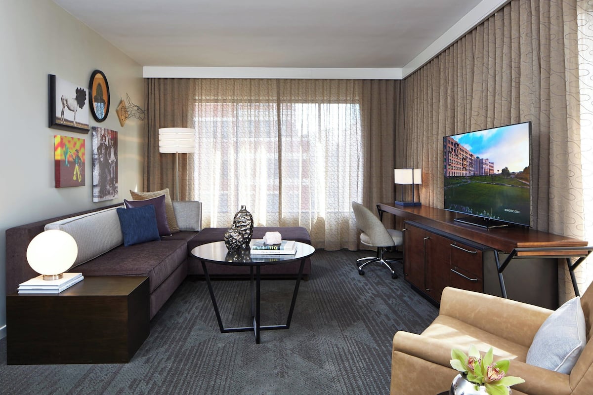 A hotel room with a sofa, a coffee table, a TV, a desk, and a lamp.