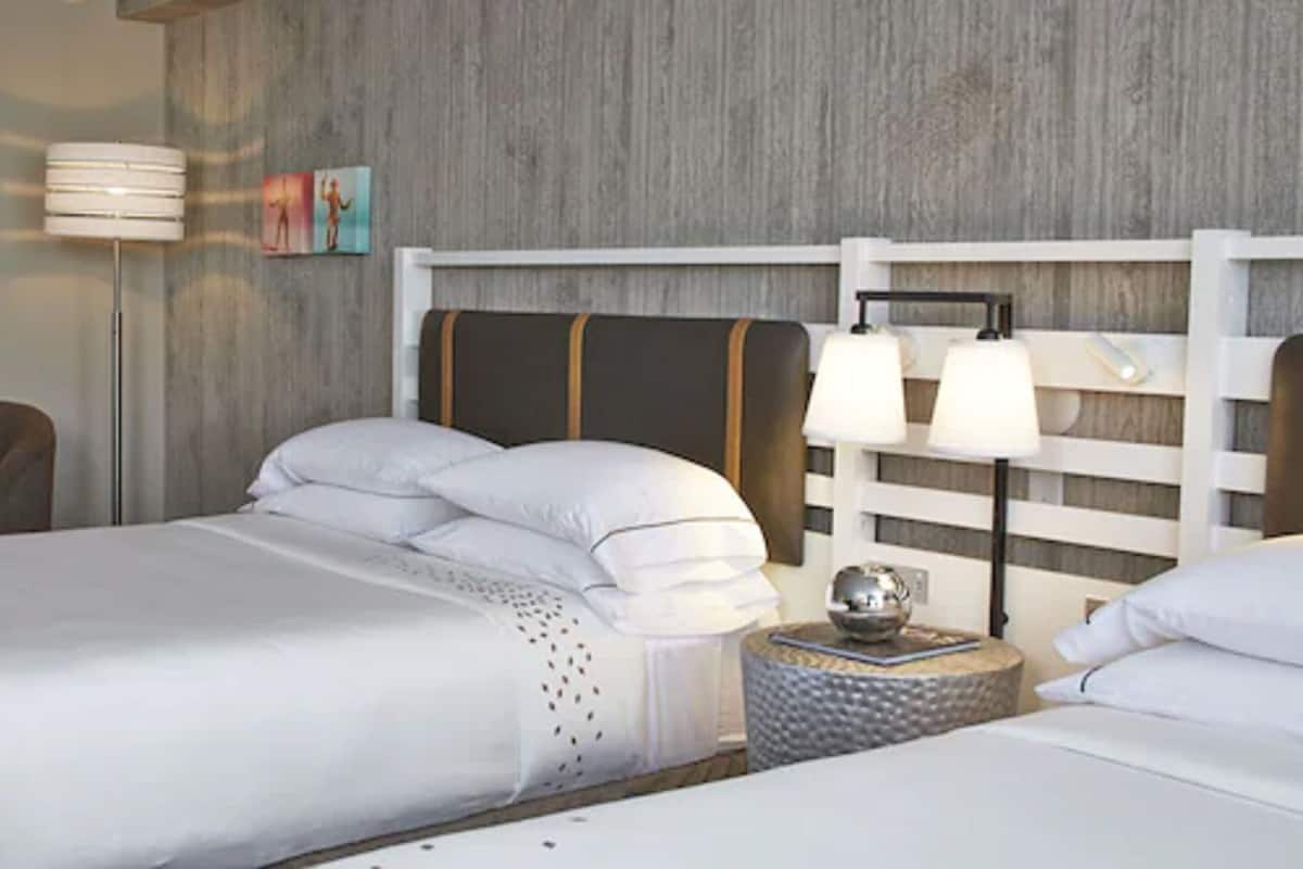 A hotel room with a bed, two bedside lamps, a round side table, and a wall-mounted artwork.