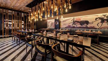 A restaurant with wooden tables and chairs, hanging light fixtures, and a mural on the wall.