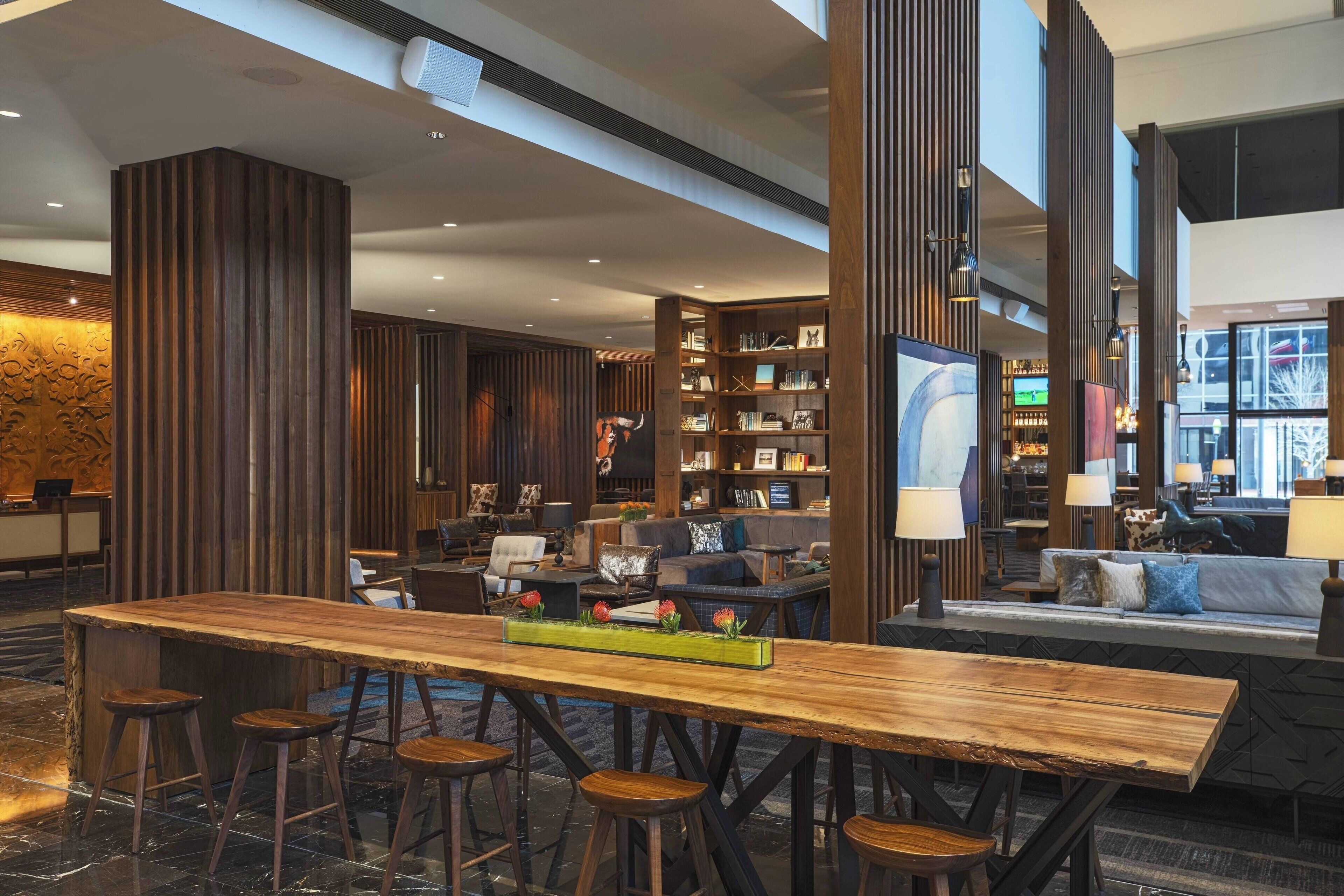 Un vestíbulo moderno con un mostrador de recepción de madera, taburetes de bar, zona de estar y una estantería.