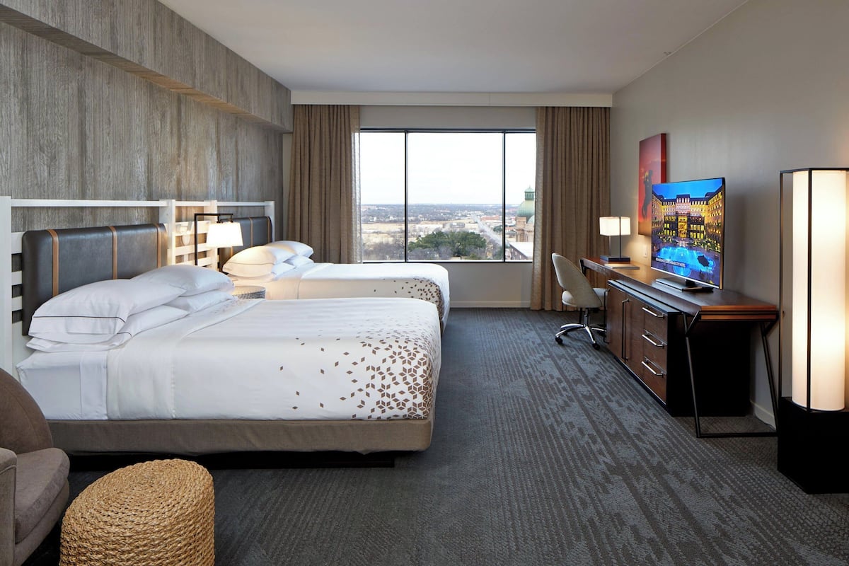 A hotel room with two beds, a desk, a chair, and a television.