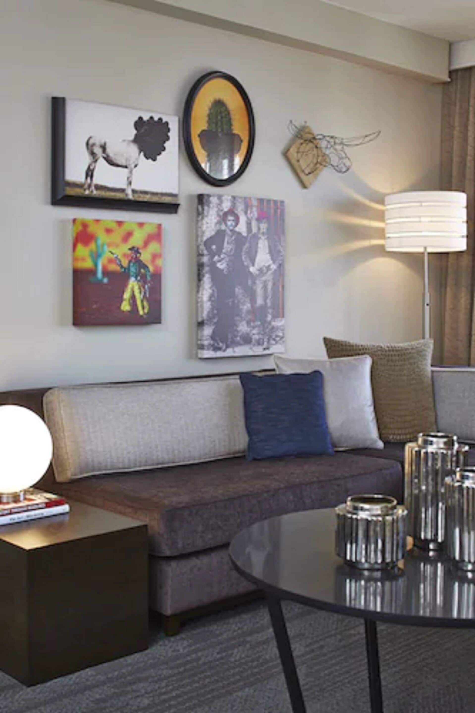 A modern living room with a sofa, a round coffee table, and wall art including a cow, a cactus, and a cowboy painting.