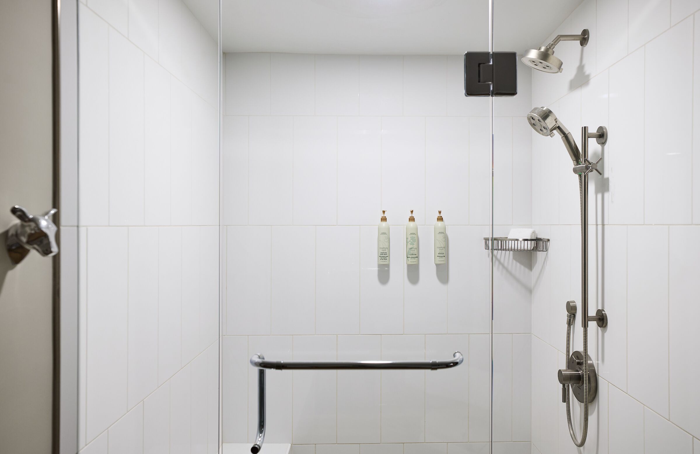 Un baño moderno con azulejos blancos, un cabezal de ducha de mano, un grifo empotrado en la pared y una barandilla.