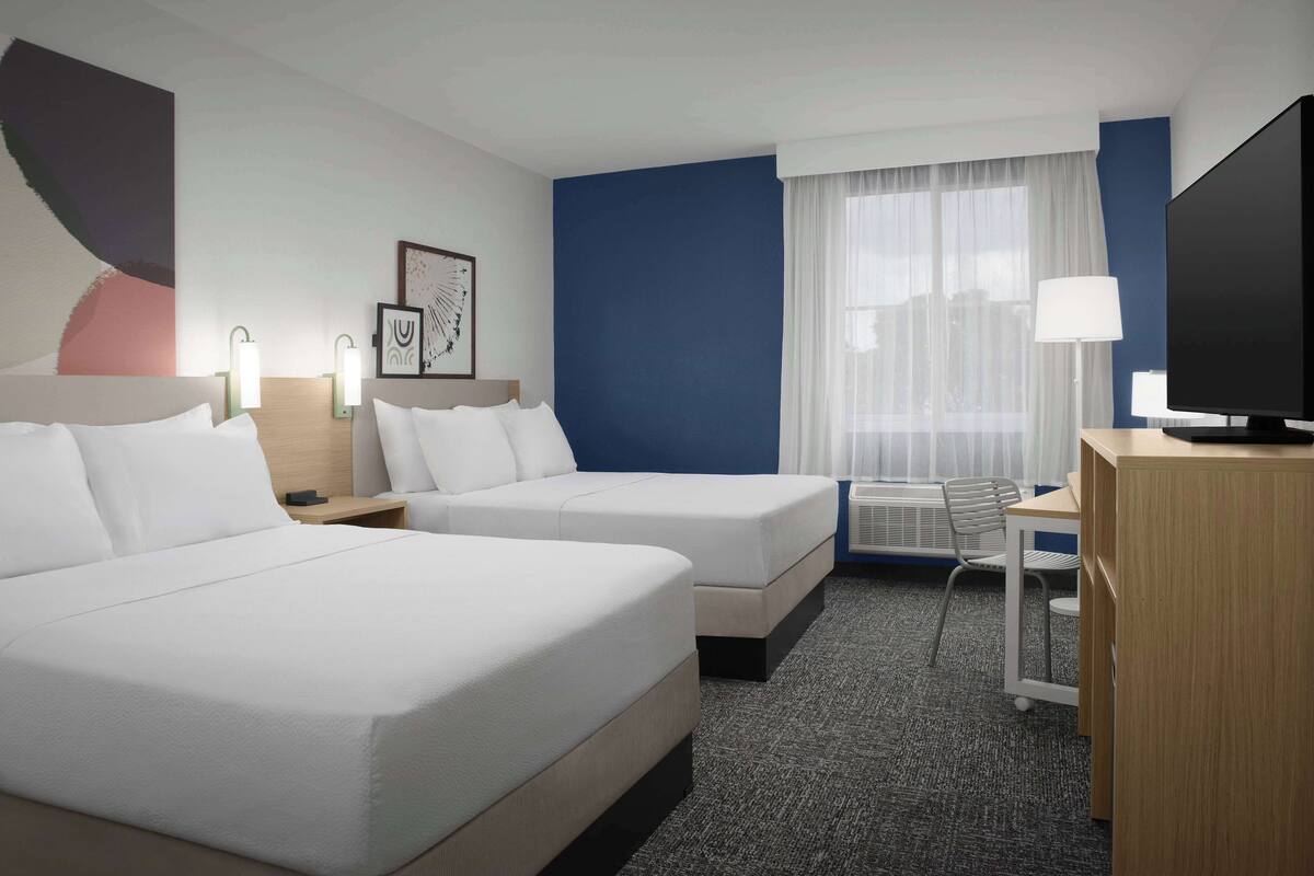 A hotel room with two beds, a desk, a chair, a television, and artwork on the walls.
