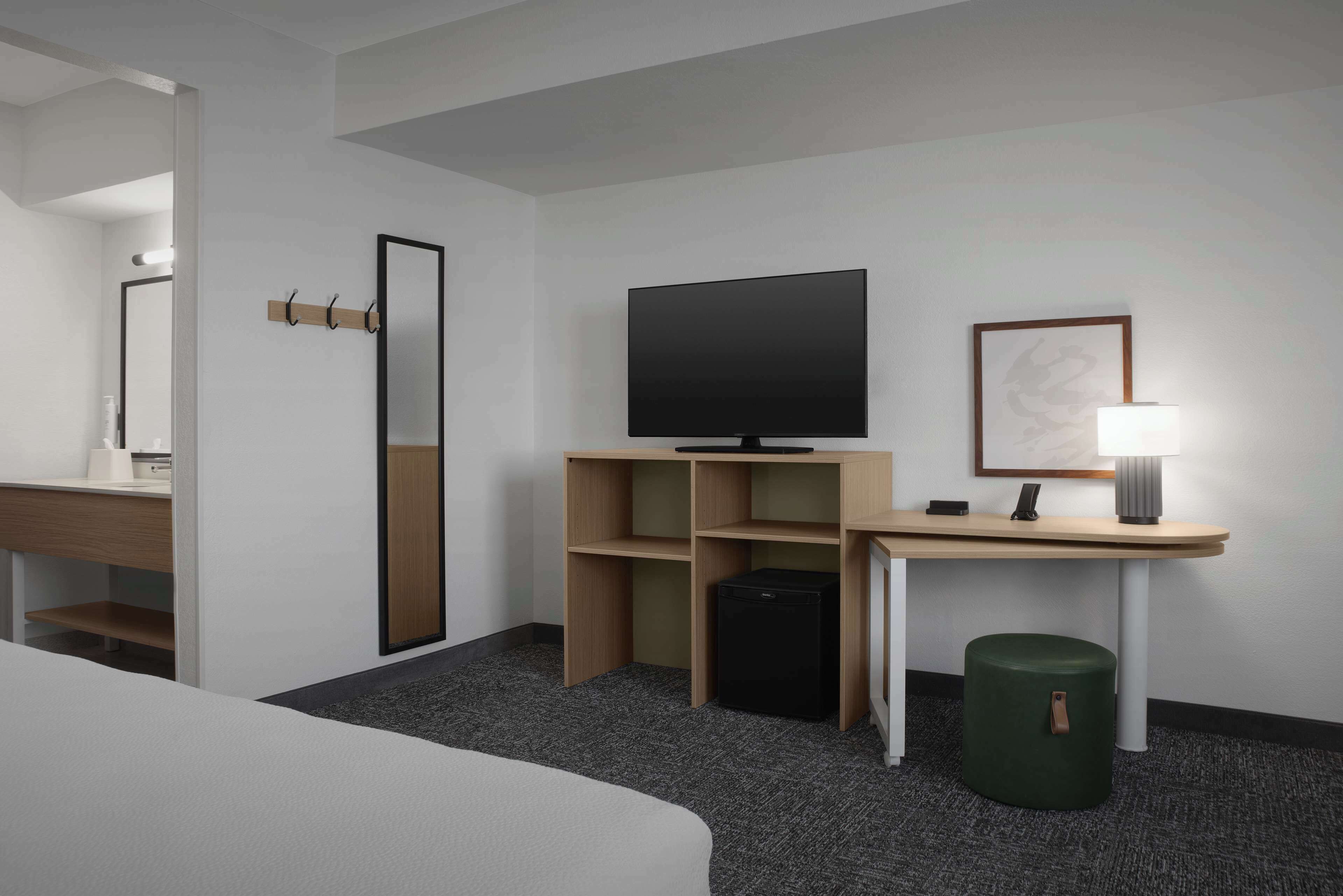 Una habitación de hotel con una cama, un escritorio, un televisor, un espejo y un pequeño cubo de basura.