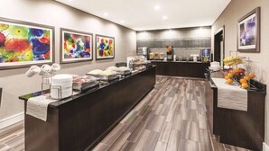 A modern hotel lobby with a reception desk, buffet area, and artwork on the walls. - La Quinta Inn & Suites by Wyndham San Antonio Downtown (San Antonio)