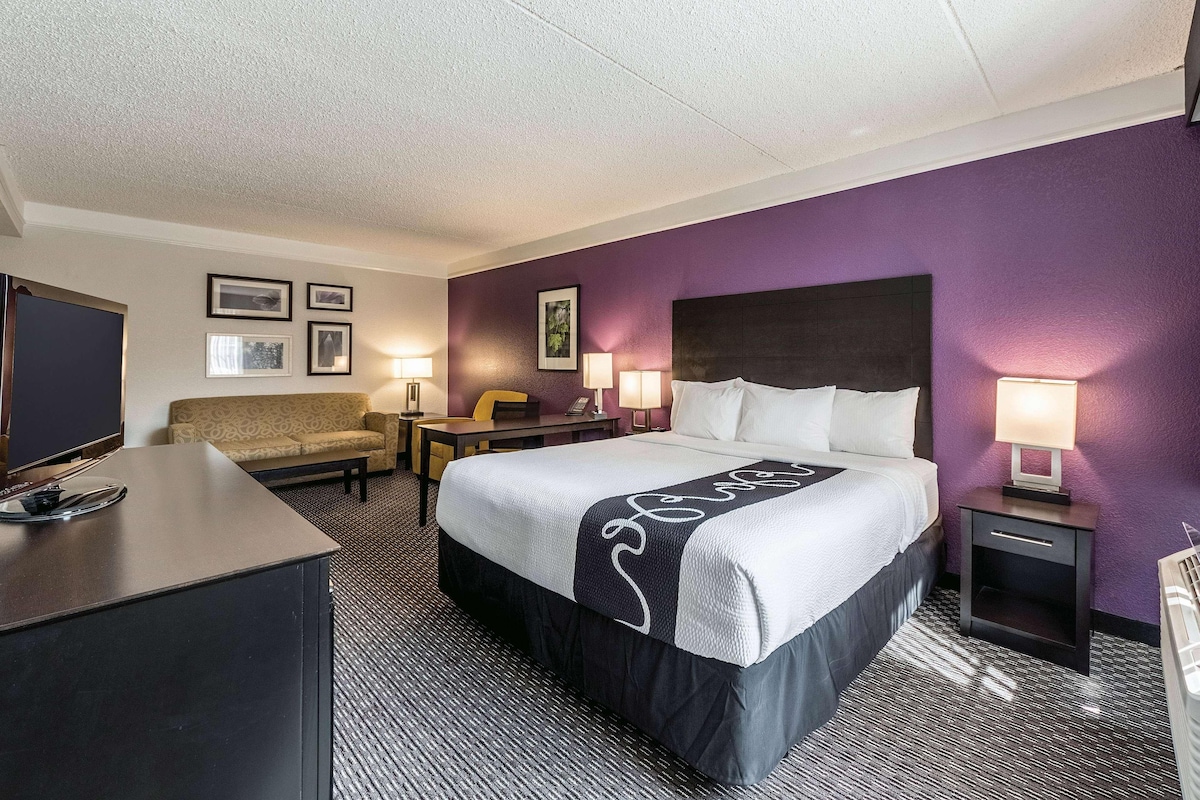 Habitación de hotel con cama, escritorio, silla, televisor y mesita de noche con lámpara.