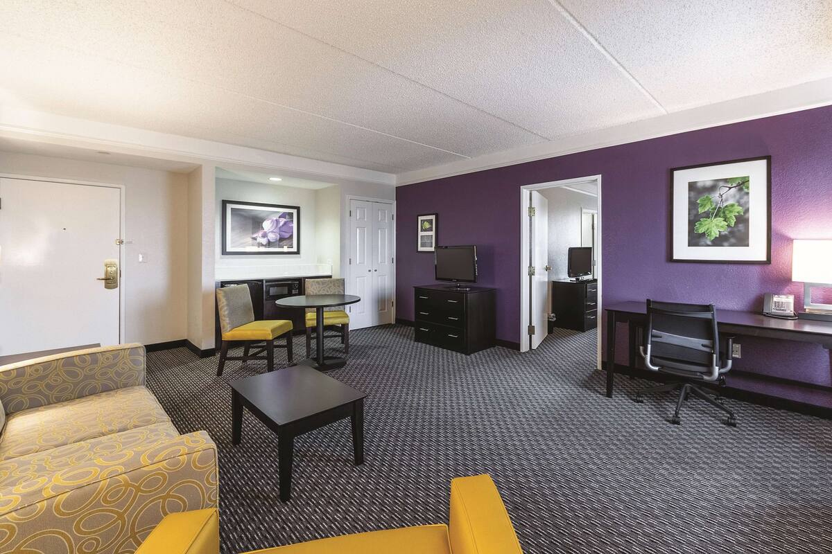 A hotel room with a sofa, a small table, a TV, a desk with a computer, and a telephone.