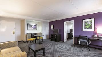 A hotel room with a sofa, a small table, a TV, a desk with a computer, and a telephone.