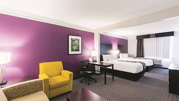 Ein Hotelzimmer mit violetter Wand, einem Bett, einem Schreibtisch, einem Stuhl und einem Sofa.