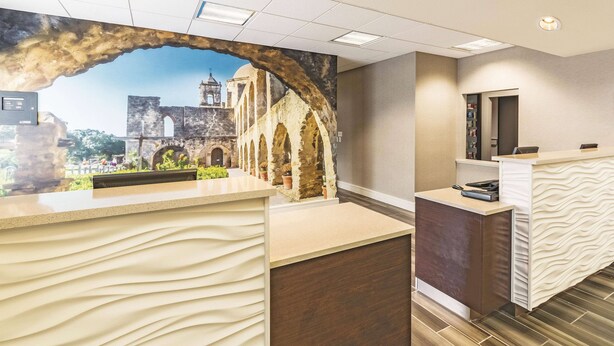 A reception area with a modern design, featuring a reception desk, a digital screen, and a view of an old building through a stone archway. - La Quinta Inn & Suites by Wyndham San Antonio Downtown (San Antonio)