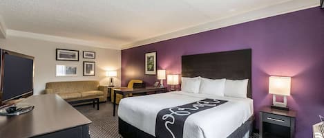 Una habitación de hotel con cama, escritorio, silla, sofá y televisión.