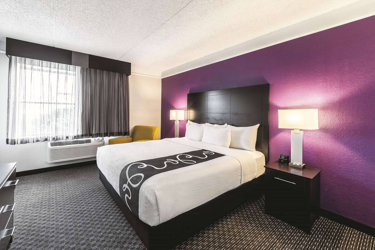 A hotel room with a bed, a chair, a desk, and a lamp.