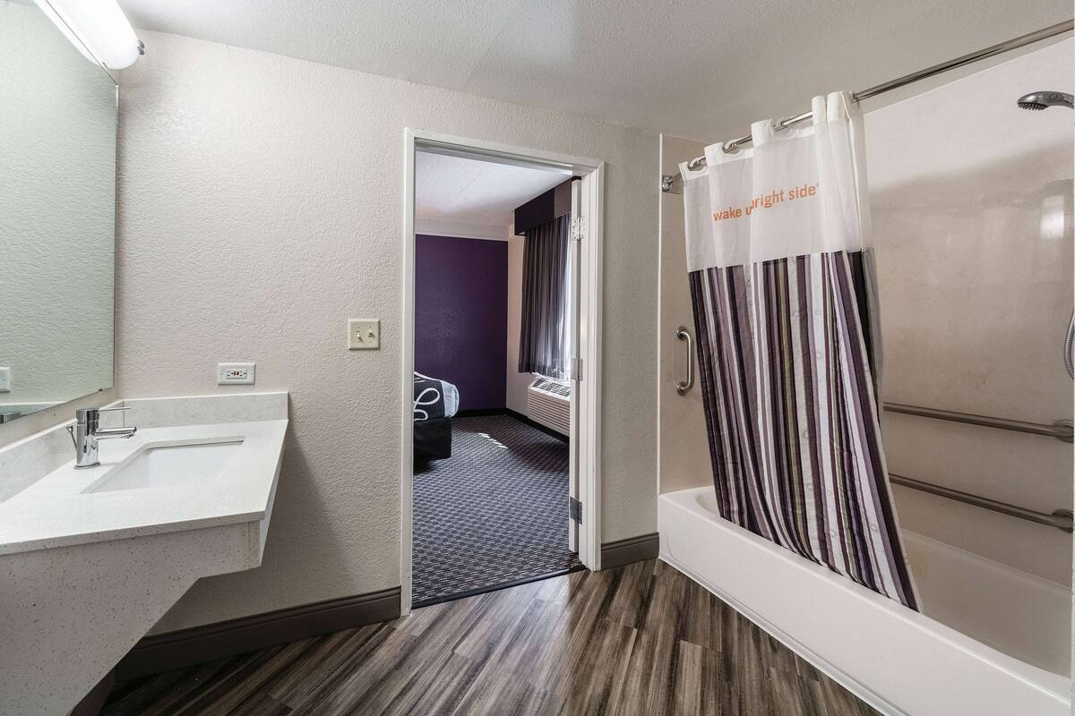 A modern bathroom with a white sink, a shower with striped curtains, and a door leading to a bedroom with purple walls.
