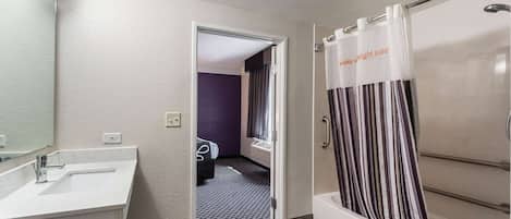 A modern bathroom with a white sink, a shower with striped curtains, and a door leading to a bedroom with purple walls.