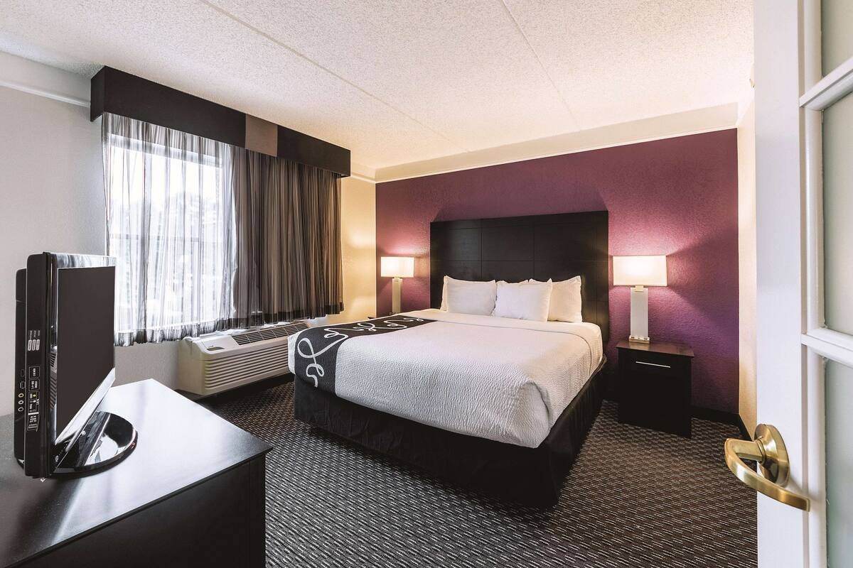 A hotel room with a bed, bedside tables, a desk with a computer, and a window with curtains.