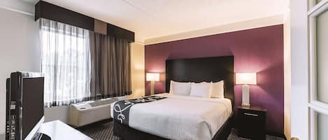 A hotel room with a bed, bedside tables, a desk with a computer, and a window with curtains.