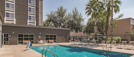 A swimming pool with lounge chairs and a building with multiple windows.