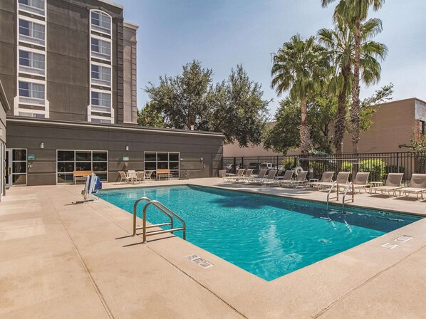Una piscina con sillas de descanso y un edificio de amplias ventanas.
