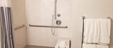 Zona de ducha con barra de apoyo, toallero y una pequeña mesa con una toalla.