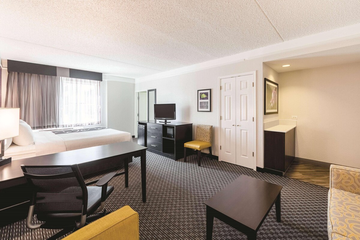 A hotel room with a bed, desk, chair, television, and a small table.