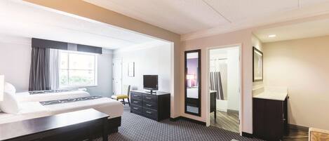 A hotel room with a bed, desk, chair, and a small table. There is a mirror, a dresser, and a door leading to a bathroom.
