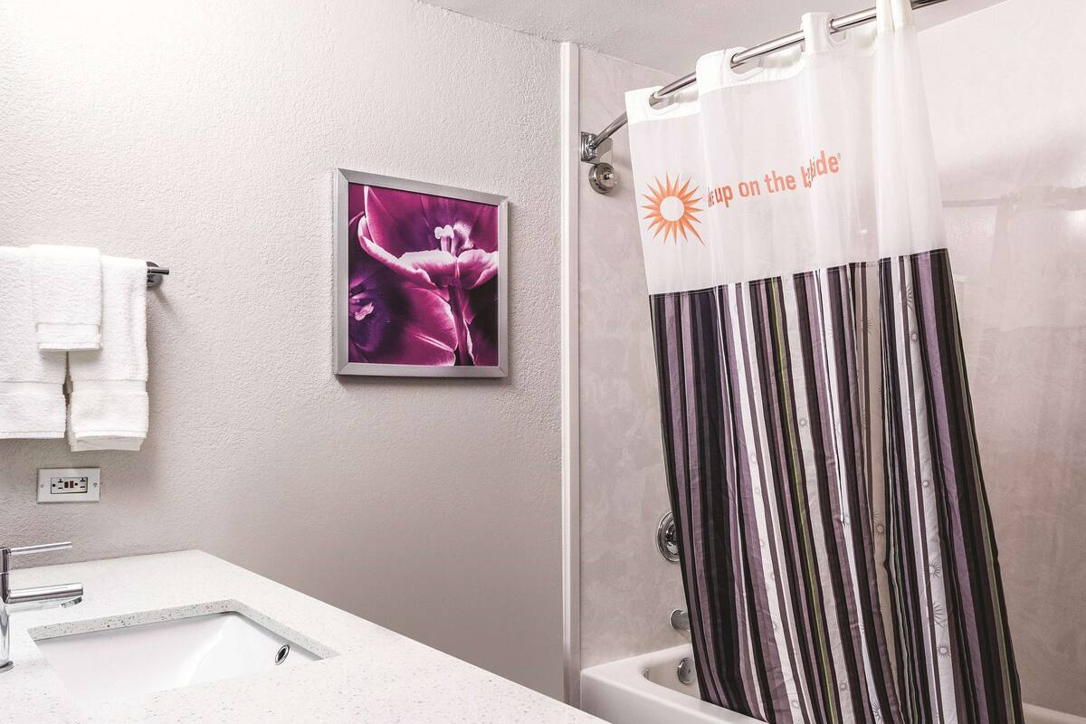 A bathroom with a shower curtain, a framed picture on the wall, and a white towel hanging on a rack.