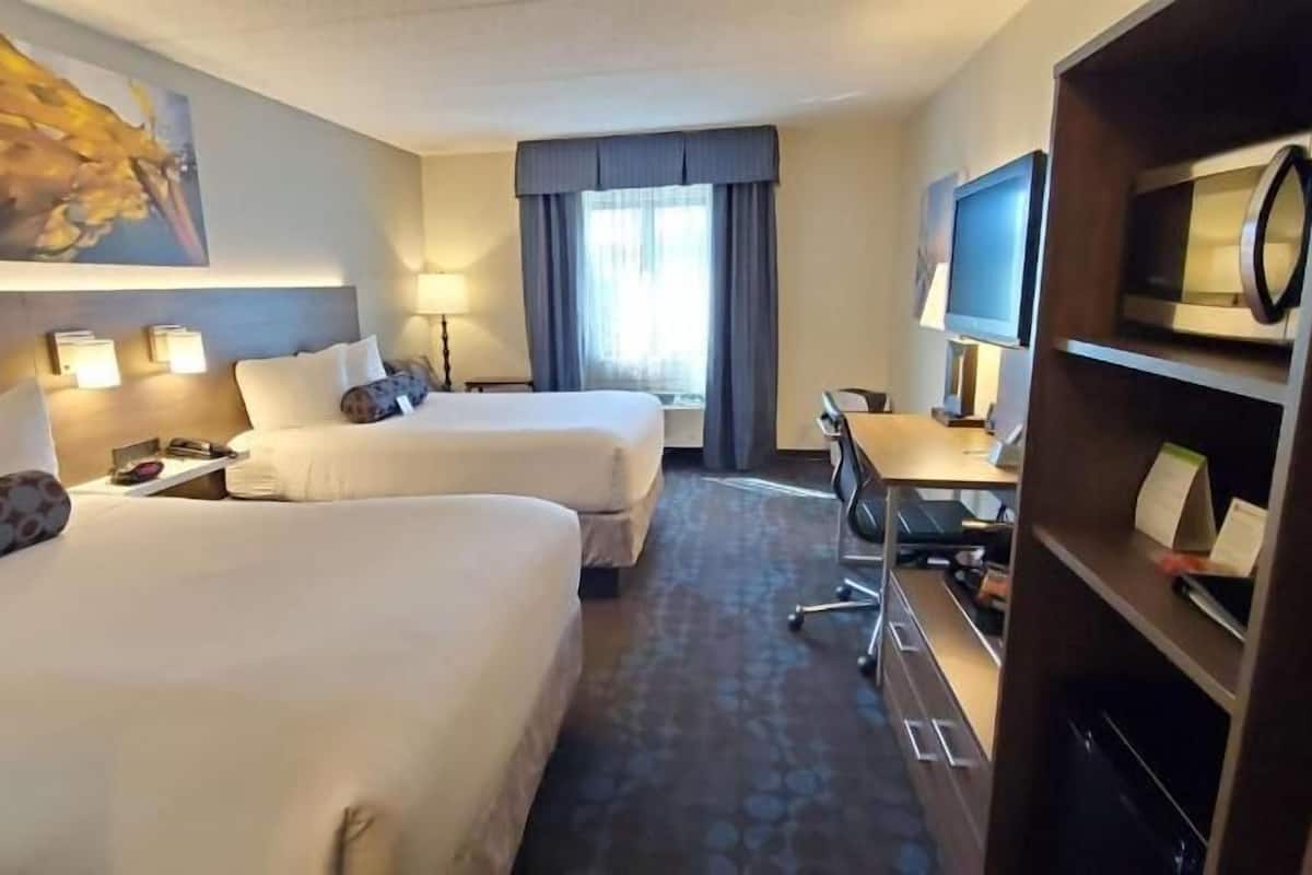 A hotel room with two beds, a desk, a TV, and a large painting on the wall.