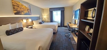 Una habitación de hotel con dos camas, un escritorio, un televisor y una estantería.