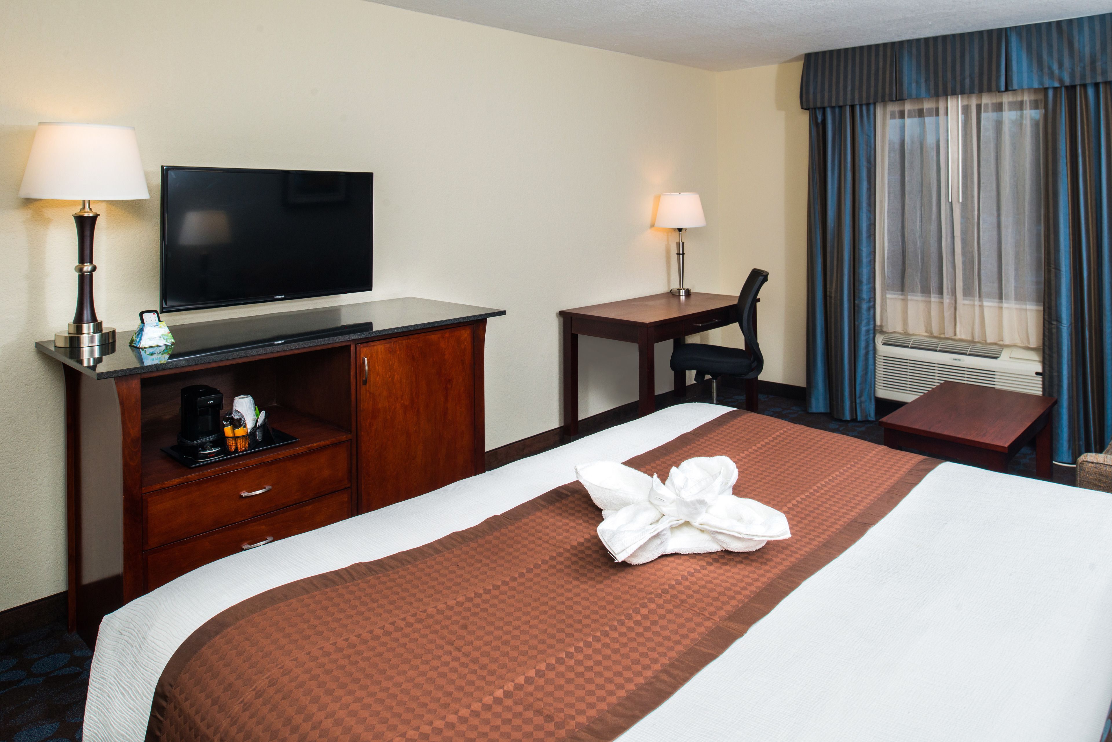 A hotel room with a bed, a TV, a desk, a chair, a coffee maker, and a window with curtains.