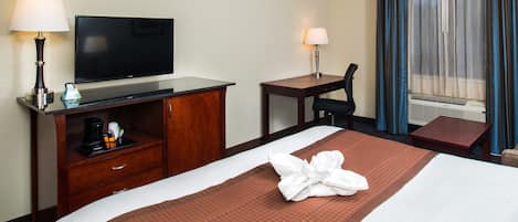 A hotel room with a bed, a TV, a desk, a chair, a coffee maker, and a window with curtains.